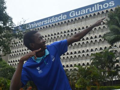 Imagem mostra aluno medalhista na frente da Instituição